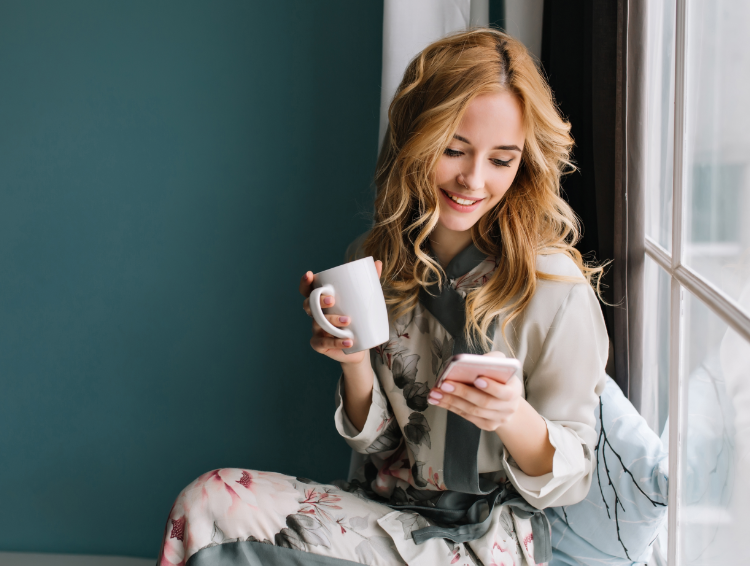 happy blonde woman holding coffee cup and smartphone